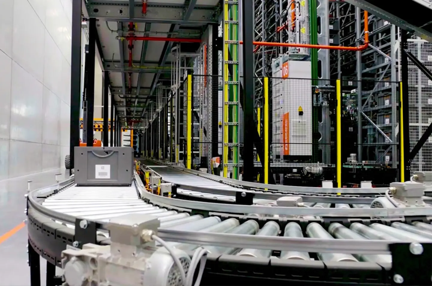 Automated warehouse conveyor system with roller tracks and safety fencing for material handling.